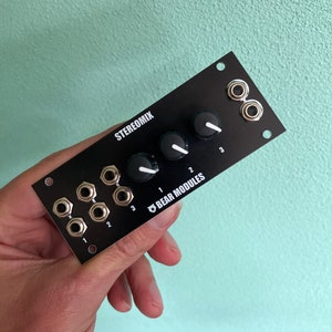 Puede incluir: Módulo mezclador estéreo negro con tres botones y tres conectores de 1/4 de pulgada etiquetados como 1, 2 y 3. El módulo está etiquetado como "StereoMix" y "Bear Modules".