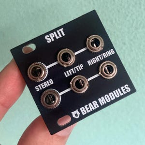 May include: Black electronic module with six silver jacks and white text that reads "SPLIT", "STEREO", "LEFT/TIP", "RIGHT/RING", and "BEAR MODULES". The module has two mounting holes.