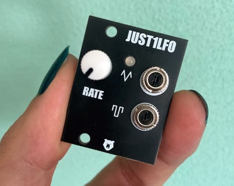 May include: A black Eurorack module with the text "JUST1LFO" printed on it. The module has a white knob labeled "RATE" and two silver jacks.