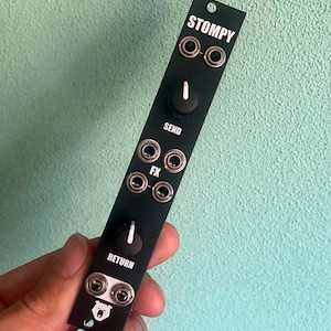 Puede incluir: Módulo de efectos StompY negro con perillas etiquetadas como "Send", "Return" y "FX". El módulo tiene un logotipo de oso y varios conectores.