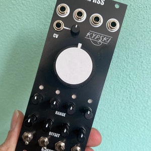 Puede incluir: Módulo electrónico negro con el texto "XXPRSS" y "KYPSKI" impreso. Cuenta con múltiples perillas, interruptores y conectores de entrada. El módulo también tiene el texto "BEAR MODULES" y "CV".