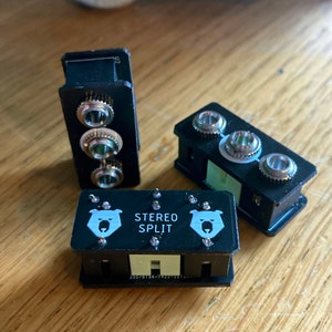 May include: A black stereo split box with two white bear logos and the text "STEREO SPLIT". The box has three silver jacks on each side.