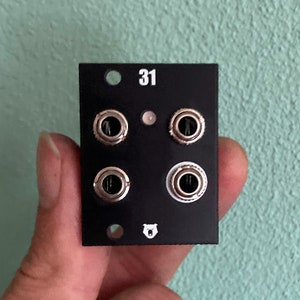 Puede incluir: Módulo Eurorack negro con cuatro jacks plateados y el número "31" impreso en la parte delantera. Un logotipo de oso blanco está impreso en el centro inferior.