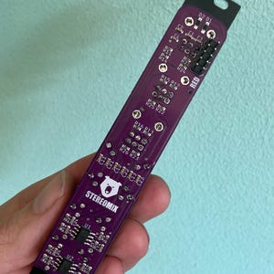 May include: A purple circuit board with the text "STEREOMIX" and a bear logo. The board has several components, including resistors, capacitors, and integrated circuits. The board is labeled with the text "RED" and "O2 01".