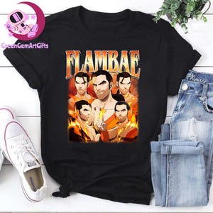 May include: Black t-shirt featuring a graphic of five men with flames and the word "FLAMBAE" in orange and white. The design is reminiscent of a vintage concert poster. The shirt is paired with blue jeans and white sneakers.
