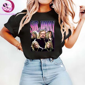May include: Black t-shirt featuring a graphic of a man with long blonde hair, with the text "SIR JIMMY Crystal" in a retro style. The shirt is worn by a person in blue jeans.