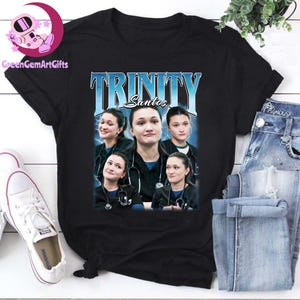 Könnte beinhalten: Eine weiße Keramik-Tasse mit schwarzem Henkel und dem Text "But First, Coffee" in fetter, schwarzer Schrift. Die Tasse steht vor einem verschwommenen Hintergrund, der eine gemütliche Umgebung suggeriert.