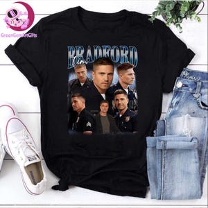 May include: Black t-shirt with a vintage-style graphic of five men in police uniforms. The graphic includes the text "Bradford Tim".