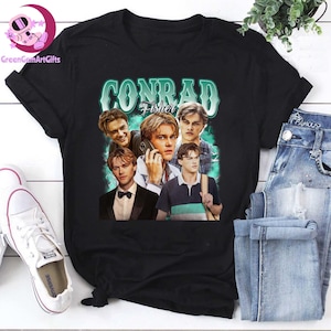 Puede incluir: Camiseta negra con un diseño gráfico verde azulado que dice "CONRAD Fisher" y presenta un collage de imágenes. Las imágenes muestran a una persona en varias poses. La camiseta se muestra con vaqueros azules y zapatillas blancas.