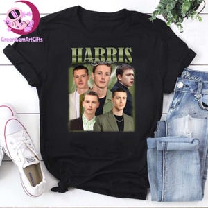 Puede incluir: Camiseta negra con un gráfico de estilo vintage de cuatro caras de hombres y el texto "HARRIS Dickinson" en una fuente verde y blanca.