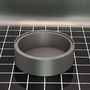 May include: A black, 3D printed, cylindrical container with a smooth, slightly textured surface. The container has a round opening at the top.