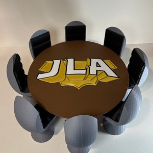 May include: A brown round table with a white "JLA" logo in the center.  The table is surrounded by seven gray chairs.