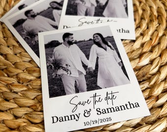 May include: Several black and white wedding announcement cards with a photo of a couple holding hands. The cards read "Save the date" and include the names "Danny & Samantha" and the date "10/19/2025". The cards are on a woven surface.