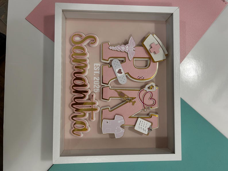 May include: A pink and gold framed sign with the text "Samantha RN Est. 2025" and various medical-themed decorations.