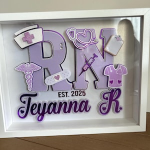 May include: A white shadow box with a purple and white 'RN' with the name 'Teyanna R' and the text 'EST. 2025' in white. The box is decorated with various medical-themed embellishments, including a stethoscope, a bandage, a syringe, and a nurse's cap.