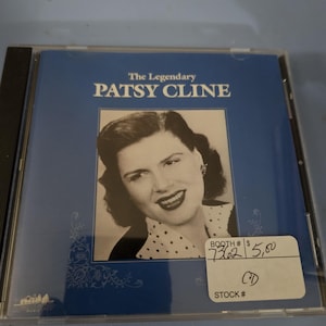 May include: A CD case featuring a blue cover with the text "The Legendary PATSY CLINE." The cover includes a black and white portrait of Patsy Cline. The CD case is in a clear plastic case.