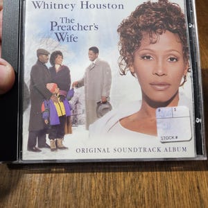 May include: A CD case featuring the album "The Preacher's Wife" by Whitney Houston. The cover art includes a portrait of Houston and a scene with actors. The text "ORIGINAL SOUNDTRACK ALBUM" is also visible.