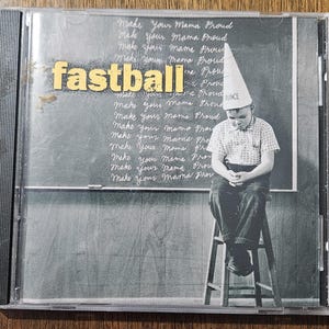 May include: CD case for the Fastball album. The cover features a black and white image of a boy wearing a dunce cap, sitting on a stool in front of a chalkboard. The words "Make Your Mama Proud" are written repeatedly on the chalkboard. The band's name, "fastball", is in yellow letters.