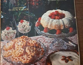 May include: A vintage cookbook titled "Nice and Easy Desserts" by Cyndee Kannenberg. The cover features a bundt cake with strawberries, a pie, and other desserts on a table. The book is from Joan Dwyer, Baird & Warner.