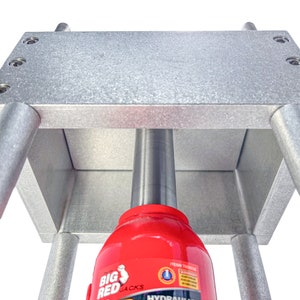 May include: A silver metal frame with a red hydraulic jack inside. The jack is labeled "Big Red Jacks" and "Hydraulic" with a white and blue logo.