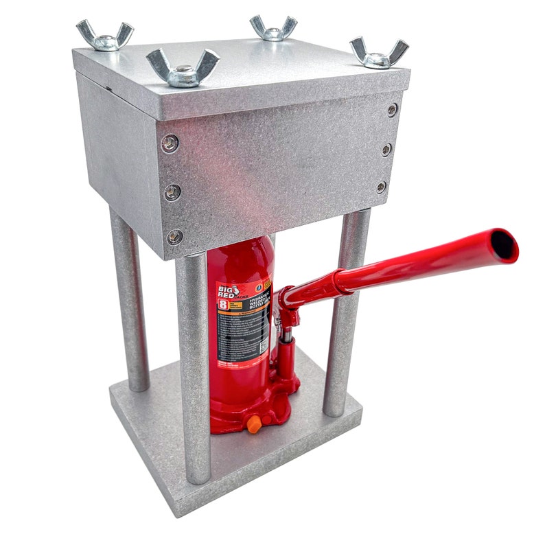May include: A metal frame with a red hydraulic bottle jack inside. The jack has a handle and a lever. The frame has a metal top with four wing nuts.