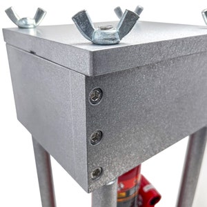 May include: A silver metal press with a red base and four wing nuts on the top. The press has a textured surface and is made of metal.