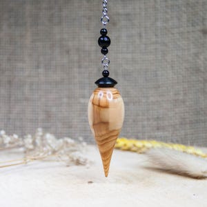 May include: A wooden pendulum with a black top and a natural wood finish. The pendulum is hanging from a silver chain with black beads.