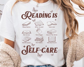 May include: White t-shirt with a brown graphic that says "Reading is Self-Care" with illustrations of books and butterflies.