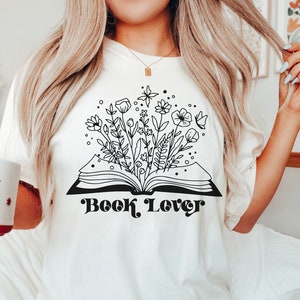 May include: White t-shirt with a black and white illustration of a book with flowers growing out of it. The text "Book Lover" is printed in black below the illustration.