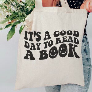 May include: A white canvas tote bag with black text that reads "It's a good day to read a book" with two smiley faces.