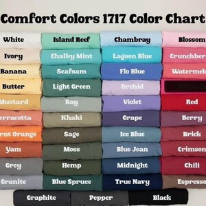 May include: Color chart of Comfort Colors 1717, featuring a variety of fabric colors. The chart displays a range of hues, including white, blue, pink, green, and brown. Each color is labeled with its name, such as "Chambray" and "Blossom".
