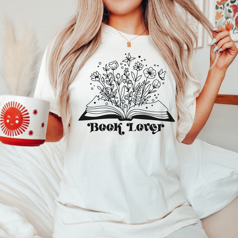 May include: White t-shirt with a black and white illustration of a book with flowers growing out of it. The text "Book Lover" is printed in black below the illustration.