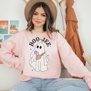 May include: A pink sweatshirt with a white ghost holding a pink drink and the text "BOO-JEE" in black.