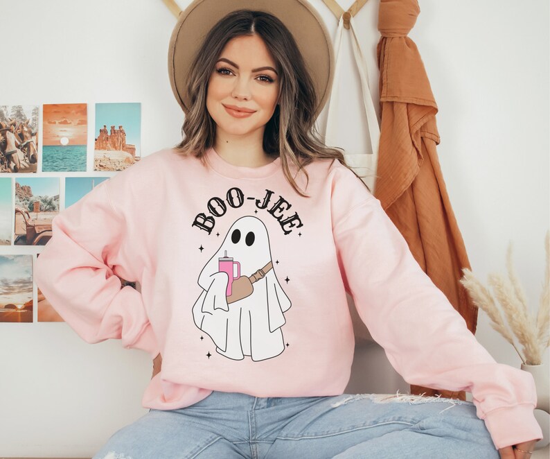 May include: A pink sweatshirt with a white ghost holding a pink drink and the text "BOO-JEE" in black.