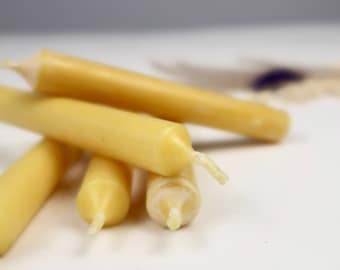 May include: A close-up of a pile of four small, yellow beeswax candles. The candles are arranged in a haphazard pile, with the wicks visible.