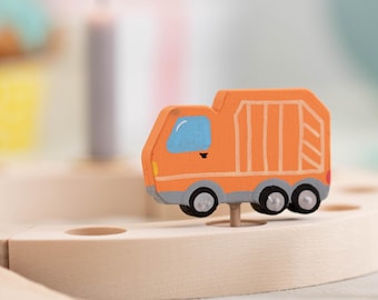 May include: Orange wooden toy truck with a gray cab and three wheels. The truck is on a wooden base with a hole in the center.