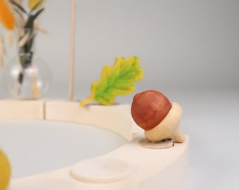 May include: A wooden autumnal wreath with a brown acorn, a green leaf, and a glass vase with dried flowers.