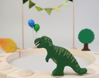 May include: A wooden toy playset with a green dinosaur, a green tree, and a colorful flag garland. The set is made of natural wood and is perfect for imaginative play.