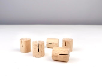 May include: Five natural wood place card holders with a slot in the top. The holders are arranged on a white surface.