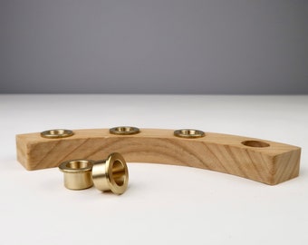 May include: A wooden candle holder with a curved shape and five brass candle cups. Two brass candle cups are laying on the table next to the holder.