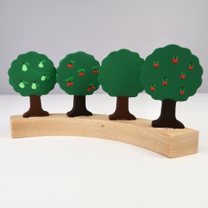 Könnte beinhalten: Vier hölzerne Spielzeugbäume mit verschiedenen Früchten darauf. Die Bäume sind grün mit braunen Stämmen und auf einer gebogenen Holzbasis angeordnet.