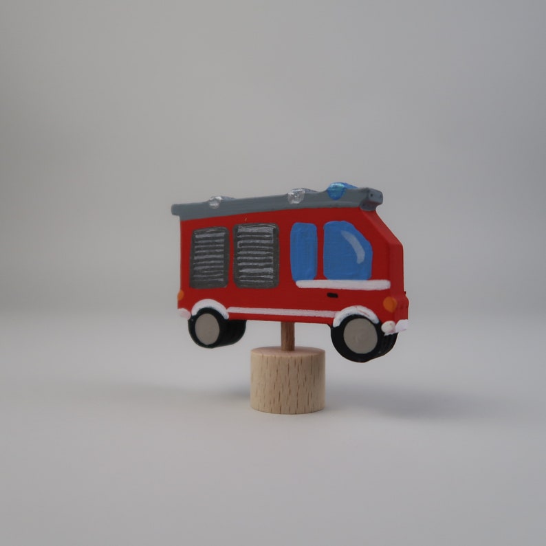 May include: A red and gray wooden toy fire truck with a blue windshield and a white base. The truck is on a wooden stand.