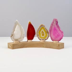 Könnte beinhalten: Vier Achat-Scheiben in verschiedenen Farben, weiß, rot, gelb und rosa, werden auf einem Holzständer präsentiert. Die Achat-Scheiben sind in einer Reihe angeordnet, wobei die weiße Scheibe links und die rosa Scheibe rechts ist.