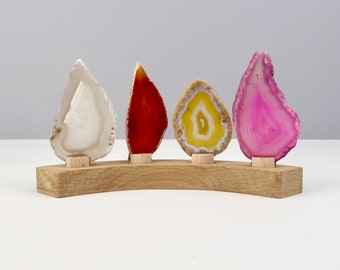 May include: Four agate slices in different colors, white, red, yellow, and pink, are displayed on a wooden stand. The agate slices are arranged in a row, with the white slice on the left and the pink slice on the right.