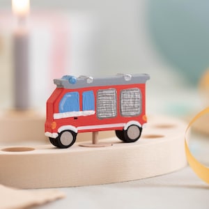 May include: A red toy fire truck with a gray ladder and blue windows sits on a wooden base. The truck is a cake topper for a birthday party.