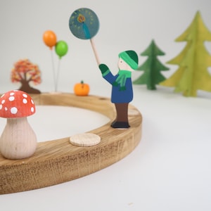 Könnte beinhalten: Ein Adventskalender aus Holz mit einem runden Sockel und verschiedenen Holzfiguren, darunter eine Person, die eine Wunderkerze hält, einen Pilz, einen Kürbis und einen Baum. Der Kalender ist mit roter, grüner, blauer und gelber Farbe verziert.
