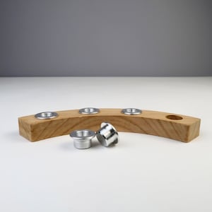 Könnte beinhalten: Ein Kerzenhalter aus Holz mit fünf Kerzenbechern aus Metall. Zwei der Becher liegen neben dem Halter auf dem Tisch.