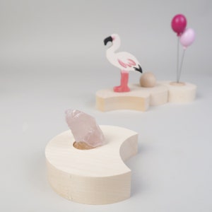 May include: A wooden stand shaped like a crescent moon with a clear quartz crystal resting in the center. The stand is made of light wood and has a smooth finish.