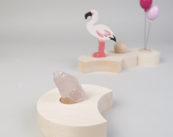 May include: A wooden stand shaped like a crescent moon with a clear quartz crystal resting in the center. The stand is made of light wood and has a smooth finish.