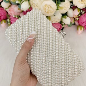 Peut inclure: Une pochette blanche en perles avec un fermoir argent&eacute;. La pochette est faite de petites perles rondes cousues ensemble en forme de losange.
